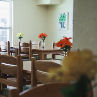 A cozy dining area with wooden tables and chairs, adorned with colorful flowers.