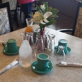 A neatly arranged dining table with cups, a vase of flowers, and condiments.