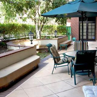 A cozy outdoor patio with furniture including a table, chairs, and an umbrella, surrounded by trees and a small garden.