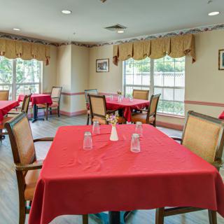 A dining room with tables covered in red tablecloths and chairs neatly arranged by the windows.