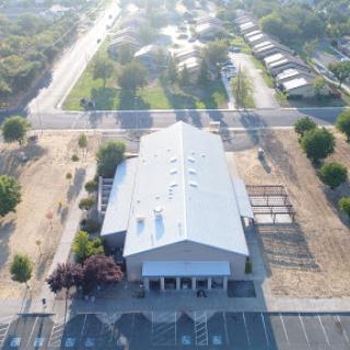 An aerial view of a community building surrounded by green spaces and a parking lot, with a road running alongside.