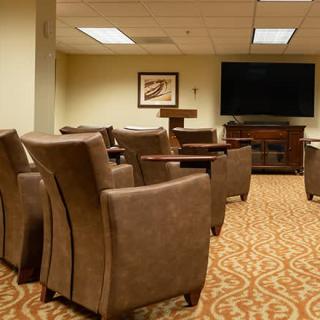 A well-furnished conference room with comfortable armchairs, a large television, and a carpeted floor setup for presentations.
