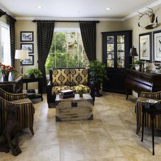 A well-decorated living room featuring elegant furniture, large windows with dark curtains, and framed artwork on the walls.