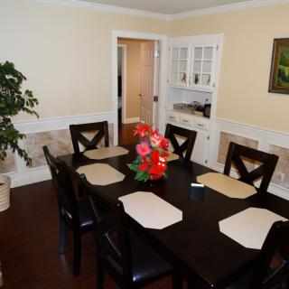 A neatly arranged dining room with a dark wooden table and chairs, featuring a floral centerpiece and placemats.