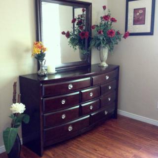 A wooden dresser with a mirror above, adorned with vases of colorful flowers in a neatly arranged room.