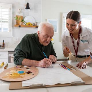 An elderly person engaging in an art activity with the assistance of a healthcare worker.