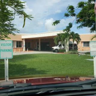 Visitor entrance of a healthcare facility with a well-maintained lawn and palm trees.