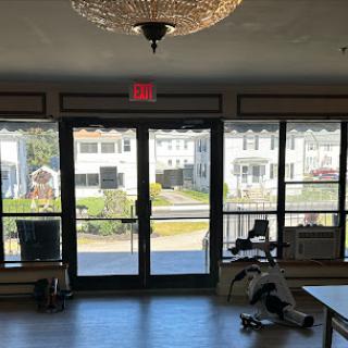 A well-lit gym area featuring exercise equipment and large windows that offer a view of the outdoors.