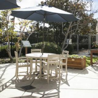 A sunny outdoor patio with a table, chairs, and a large umbrella.