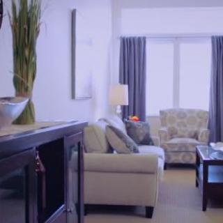 A modern living room with a comfortable sofa and armchair, centered around a coffee table, with large windows and elegant decor.