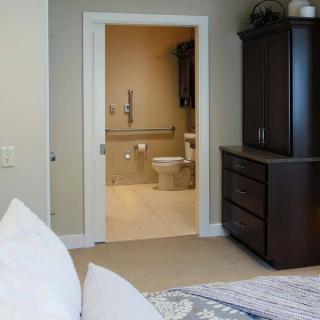 A view of a bedroom leading into an accessible bathroom with a safety handrail.