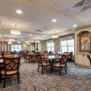 A spacious and elegantly decorated dining room with multiple tables and chairs arranged neatly, featuring large windows that allow natural light to fill the room.