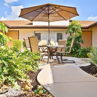A serene outdoor patio area with comfortable seating and a large umbrella, surrounded by lush greenery.