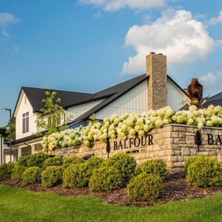 A scenic view of a beautifully landscaped entrance with blooming flowers and a building in the background.