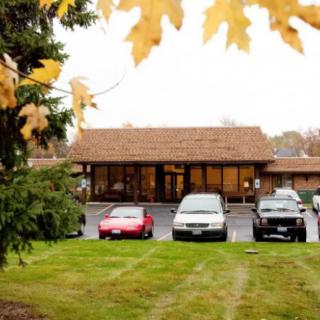 A quaint building with a parking lot in front, surrounded by autumn foliage.