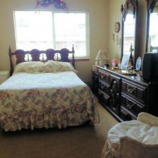 A cozy bedroom with a bed and dresser set, featuring a floral bedspread and a mirror reflecting natural light from the window.