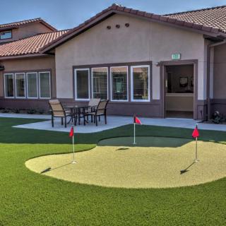 A backyard with a putting green and patio furniture in front of a house.