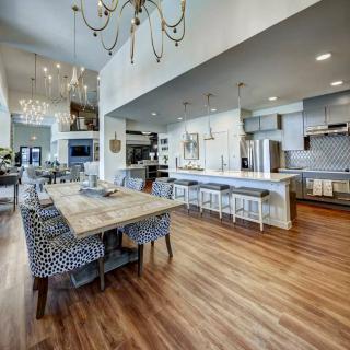 A spacious modern kitchen and dining area featuring an open concept design with hardwood floors, elegant chandeliers, and a large dining table.