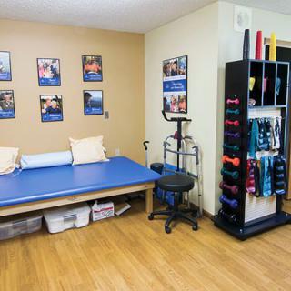 A physical therapy room equipped with a treatment table, exercise equipment, and motivational posters.