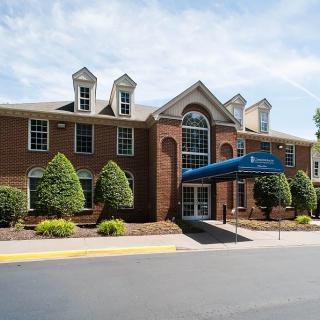 A brick hotel with a blue awning over the entrance, surrounded by well-maintained landscaping.