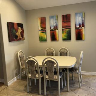 A cozy dining room with a table and six chairs, decorated with colorful abstract artworks on the walls.