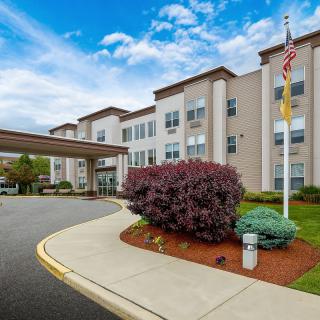 Exterior view of a hotel building with a driveway, landscaping, and flagpole.
