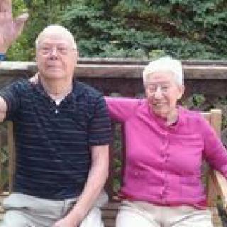 An elderly couple sitting on a bench outdoors, enjoying a moment together.