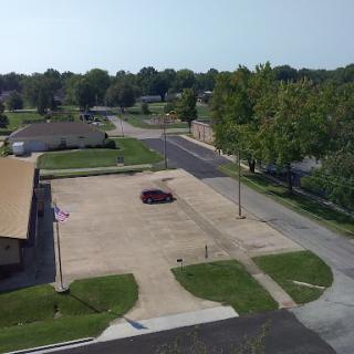 An aerial view of a quiet parking lot surrounded by greenery and a few buildings.