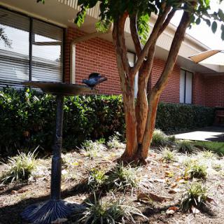 A peaceful garden scene featuring a tree, flowers, and a building in the background.
