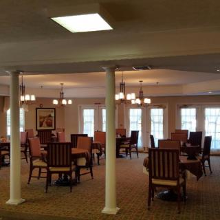 A spacious dining room with multiple tables and chairs, elegantly lit by chandeliers.