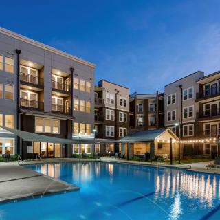 A modern apartment complex with a well-lit swimming pool during the evening.