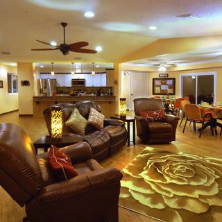 A spacious open-concept living area featuring leather sofas, a decorative rug, and modern lighting, seamlessly connecting to the kitchen and dining space.