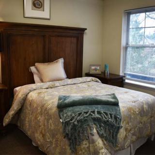 A cozy bedroom with a wooden bed frame and decorative bedding, featuring a window with a view of trees.