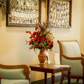 A cozy waiting area featuring elegant chairs, a decorative flower arrangement, and framed photographs on the wall.