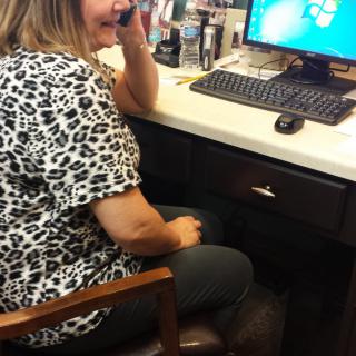A woman in an office talking on the phone while using a computer.
