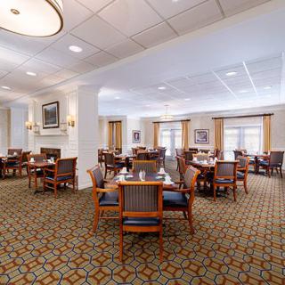 A spacious dining area with neatly arranged tables and chairs, featuring elegant lighting and patterned carpeting.