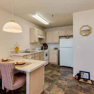 A cozy apartment kitchen with a small dining area, featuring modern appliances and a tiled floor.