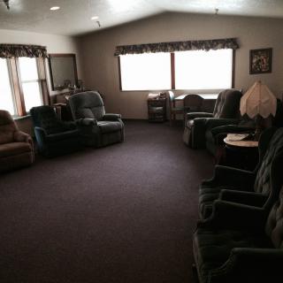 A cozy living room with several upholstered chairs arranged around the carpeted space, illuminated by natural light from large windows.