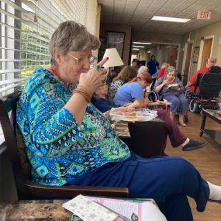 An elderly woman enjoying a meal in a lively community center setting.
