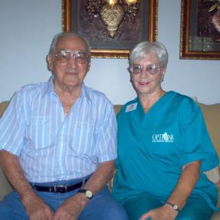 An elderly couple sitting together on a couch in their living room, smiling for the camera.