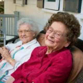 Two elderly women sitting and smiling outdoors.