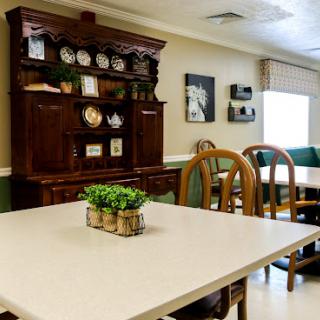 A cozy dining area featuring a wooden cabinet, a simple table, and comfortable chairs, accented with decorative plants.