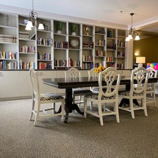 A cozy dining room with a long table, surrounded by chairs, adorned with pendant lights and lined with bookshelves.