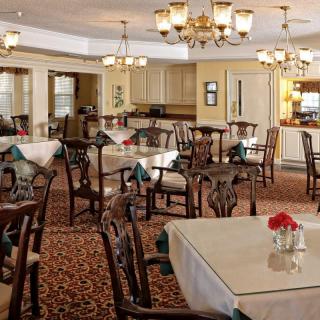 A spacious and elegantly decorated dining room with multiple tables and chairs, warm lighting, and chandeliers.