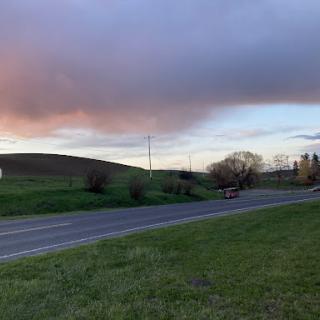 A serene view of a winding road surrounded by lush hills and a colorful sky at sunset.