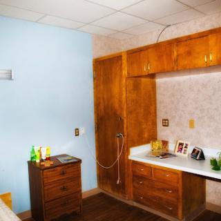 A well-lit hospital room featuring wooden cabinets and a standard hospital bed.