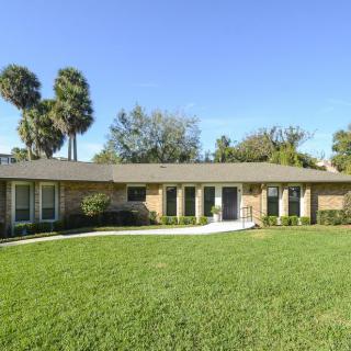 A one-story suburban house with a large lawn and palm trees in the background.