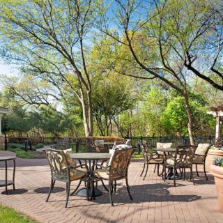 A tranquil outdoor patio area with tables and chairs surrounded by lush greenery.