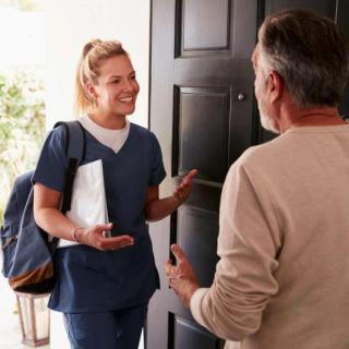 A nurse visiting an elderly man at his home, engaging in a friendly conversation at the front door.