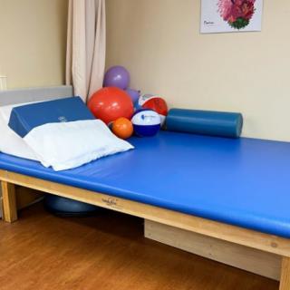 A physical therapy treatment room equipped with a blue padded table and various exercise balls.